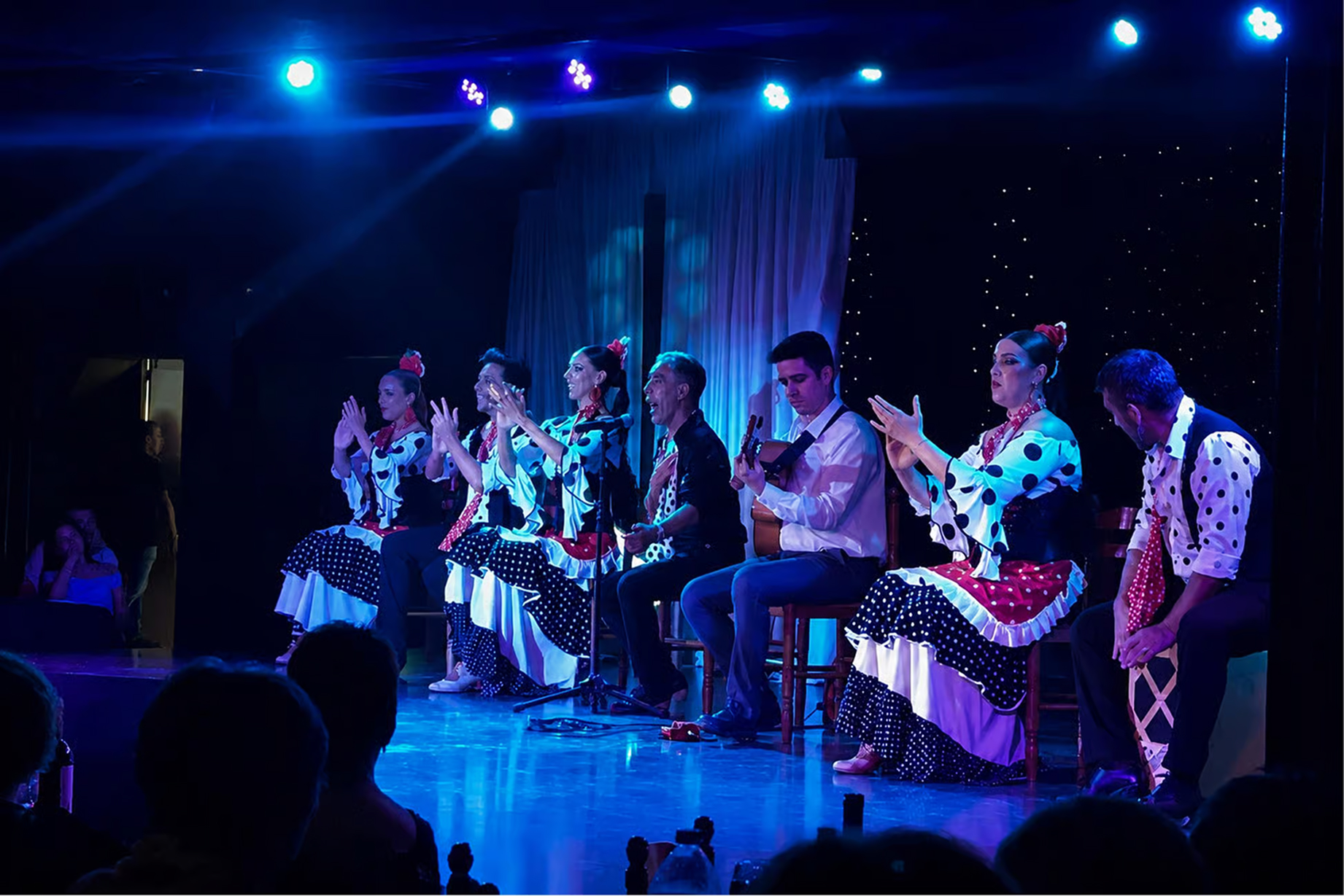 Artistas y guitarrista durante el espectáculo de La Masia Tordera, bajo la iluminación azul del escenario.